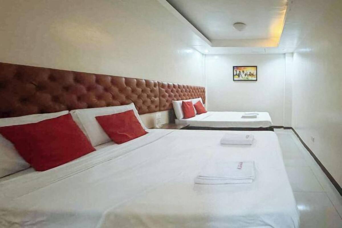 A hotel room with two beds, each with white linens and red pillows.