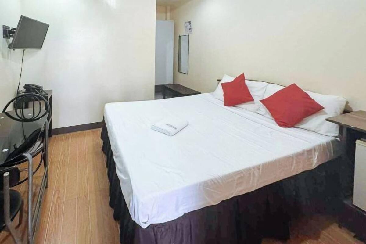 A hotel room with a bed, a desk, a chair, and a flat-screen TV.