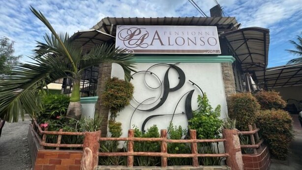 Schild für 'Pensione Alonzo' mit dekorativer Wand und Pflanzen.