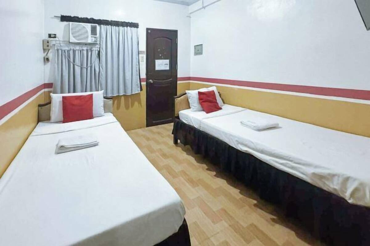 A room with two single beds, a door, an air conditioning unit, and a window with curtains.
