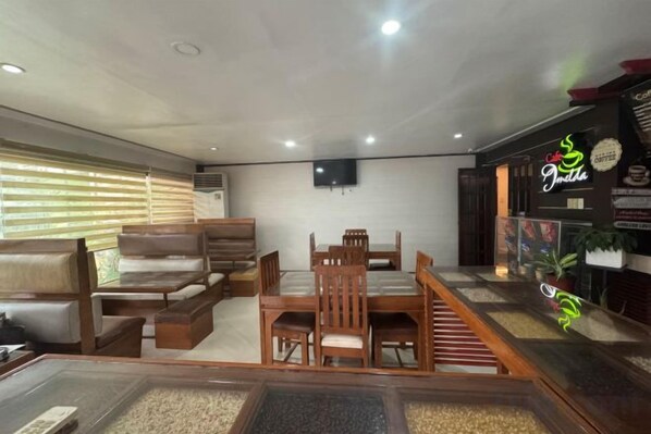 A room with a sofa, a dining table with chairs, a TV mounted on the wall, and a neon sign on the right. - Pensionne Alonso by RedDoorz (General Santos)