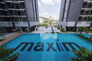A swimming pool with the word 'maxim' spelled out in the water, surrounded by modern buildings and a clear sky. - MAXIM BY FEEL HOME (Kuala Lumpur)