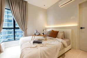 A bedroom with a bed, a bedside table, a window with curtains, and a view of buildings. - MAXIM BY FEEL HOME (Kuala Lumpur)