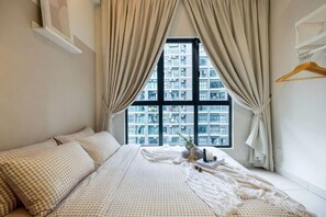Un dormitorio con un ventanal grande, una cama con ropa de cama a cuadros y una mesita de noche con lámpara.