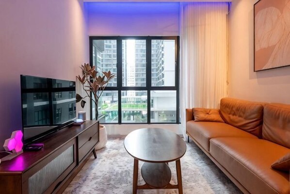 Una sala de estar con televisor, sofá y un amplio ventanal con vistas a la ciudad.