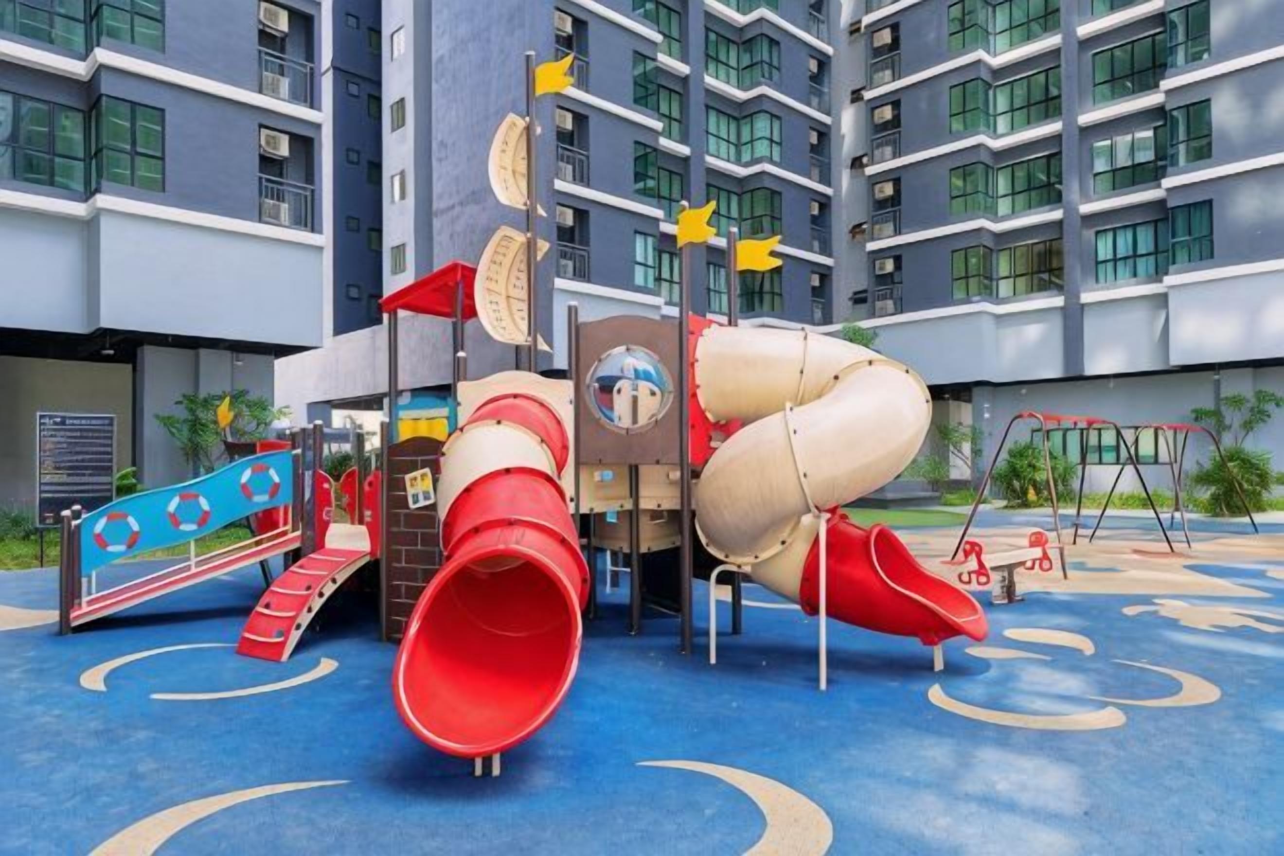 A playground with slides and climbing structures, located in front of a modern building with multiple floors and balconies.