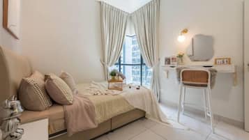 A bedroom with a bed, a bedside table, a chair, a window with curtains, and a wall-mounted shelf with a mirror.