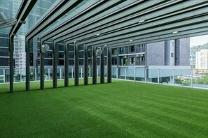 A modern building with a glass facade, a green artificial lawn, and a view of the cityscape. - MAXIM BY FEEL HOME (Kuala Lumpur)