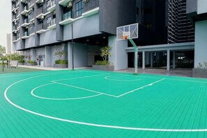 Una cancha de baloncesto al aire libre con un aro, rodeada por un edificio con balcones y ventanas.
