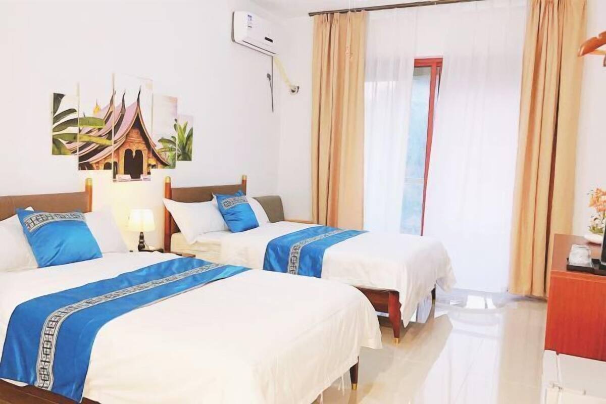 A hotel room with two beds, a desk, a lamp, and a painting on the wall.