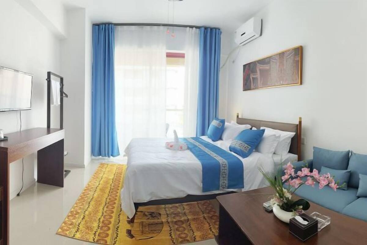 A hotel room with a bed, a sofa, a TV, a desk, and a window with curtains.
