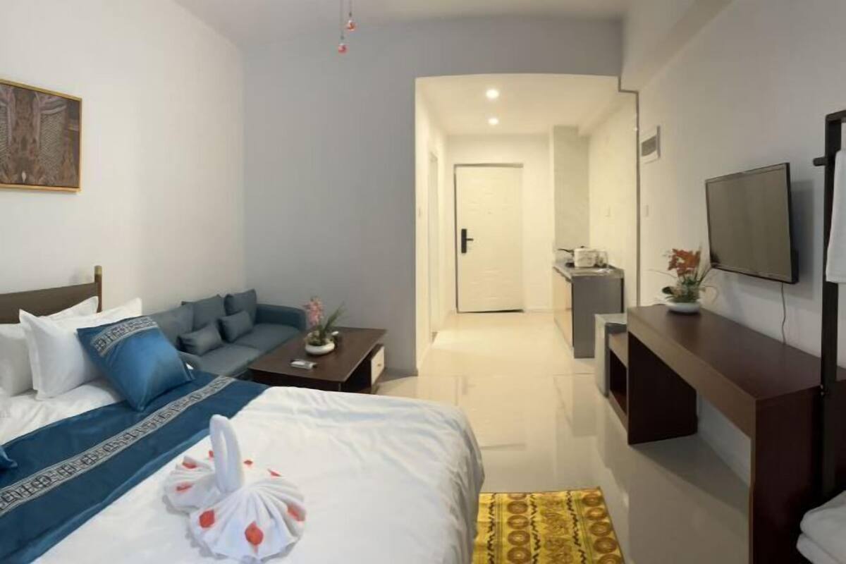 A hotel room with a bed, a sofa, a desk, a TV, and a bathroom visible through an open door.