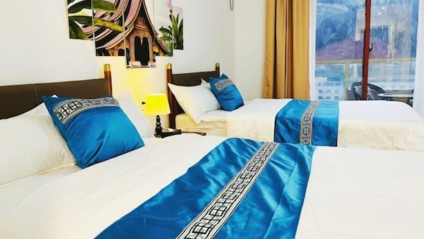 A hotel room with two beds, a nightstand, a lamp, and a window with a view. - Boten YouJia Residential Hotel (Nateuy)