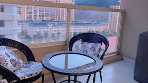 A balcony with two wicker chairs and a glass table, overlooking a cityscape with modern buildings and a mountain in the distance. - Boten YouJia Residential Hotel (Nateuy)