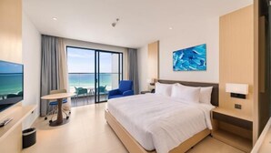 A modern hotel room with a large bed, a desk with a chair, a TV, and a balcony with a view of the sea. - The Arenam Cam Ranh Nha Trang Resort (Cam Ranh)