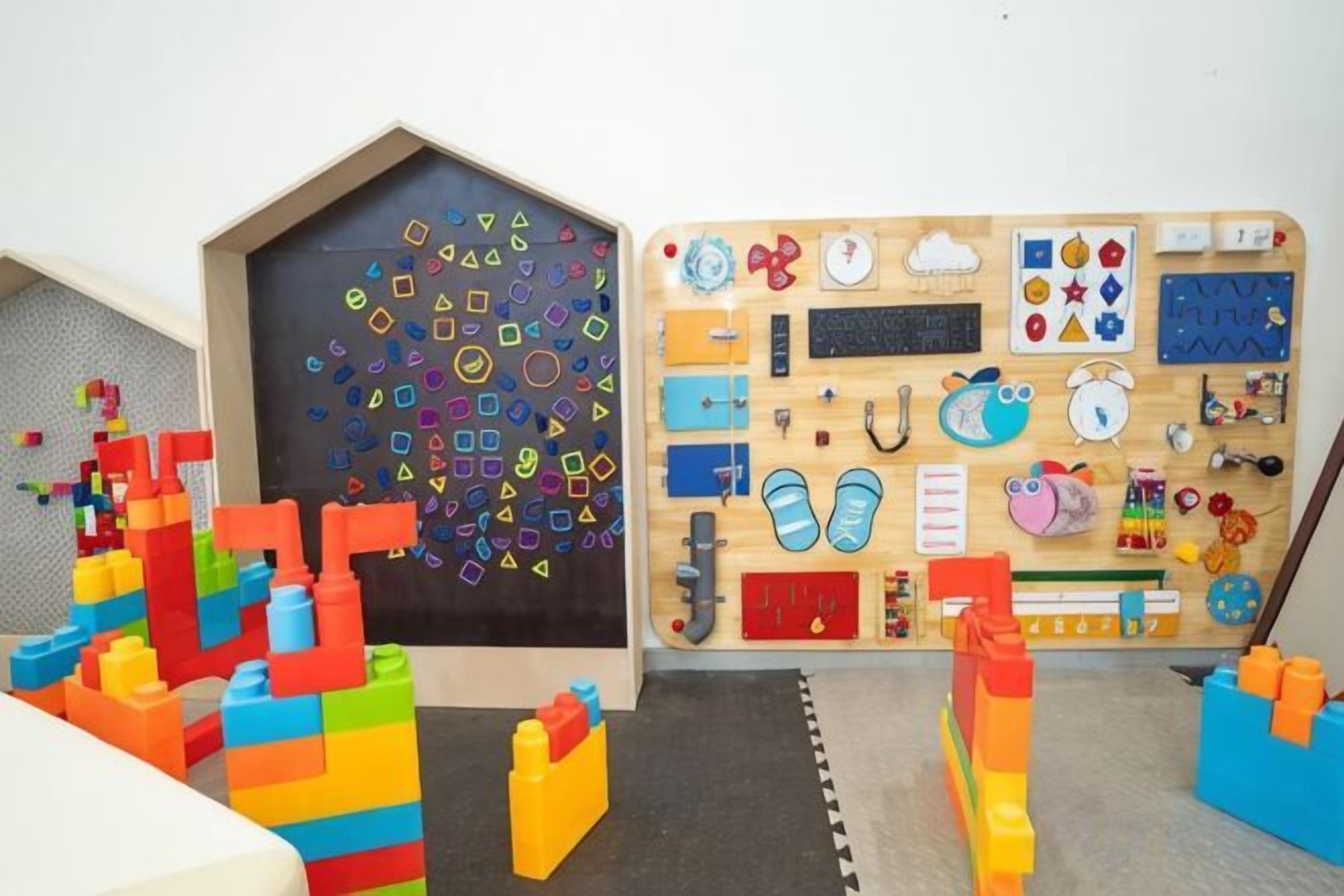 Una sala de juegos con bloques de construcción coloridos, una tabla de madera con diversas herramientas educativas y un pequeño zapatero.