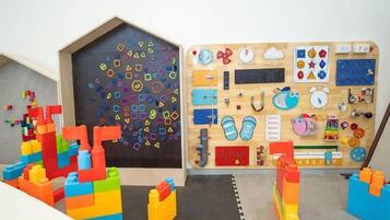 Una sala de juegos con bloques de construcción coloridos, una tabla de madera con diversas herramientas educativas y un pequeño zapatero.