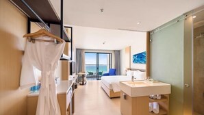 A hotel room with a bed, a bathroom with a sink and mirror, a robe hanging on a rack, and a view of the sea through the window. - The Arenam Cam Ranh Nha Trang Resort (Cam Ranh)
