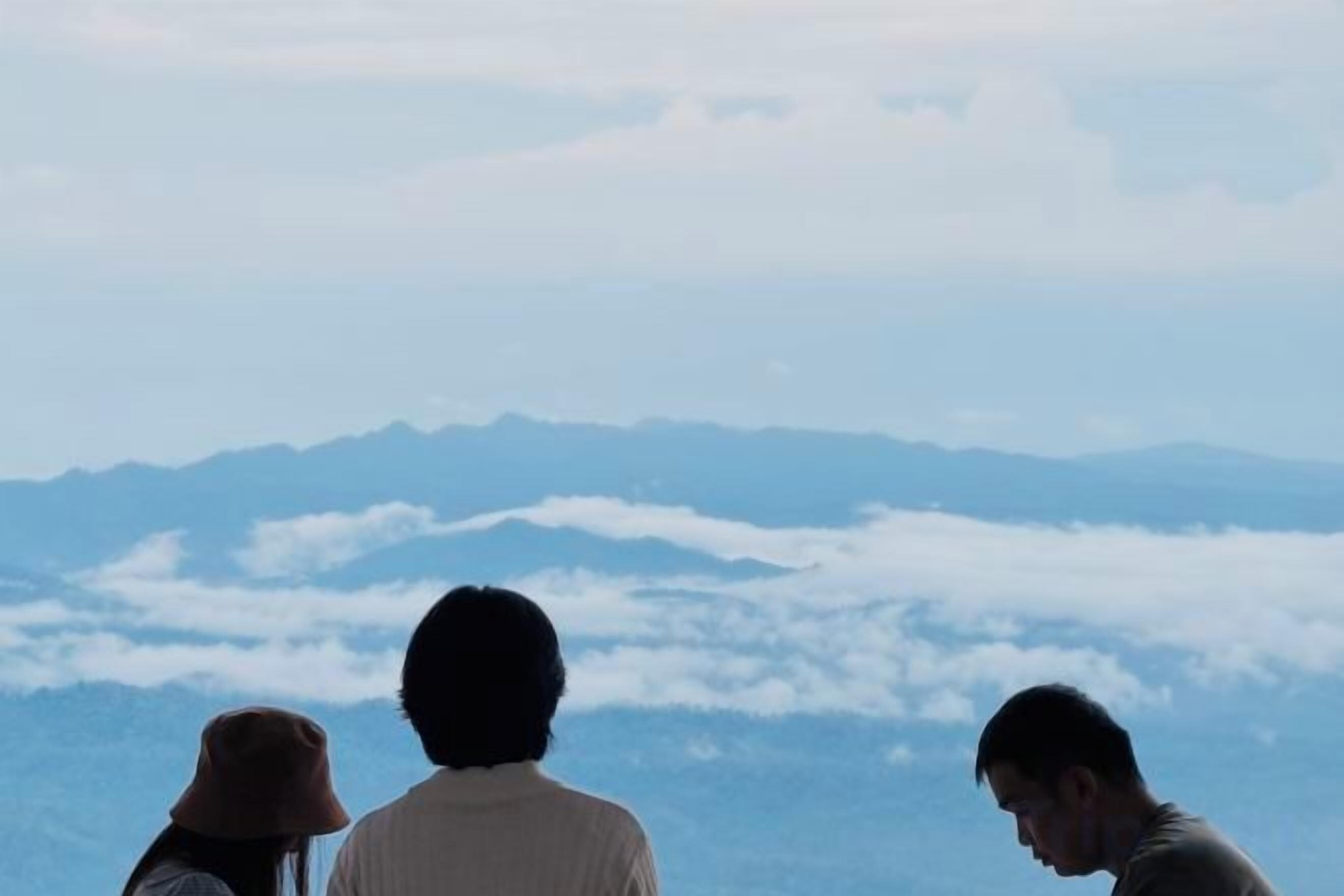 Tres personas observando un paisaje montañoso con nubes abajo.