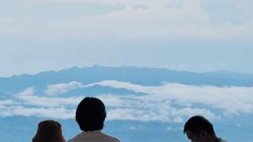 Três pessoas contemplando uma paisagem montanhosa com nuvens abaixo.
