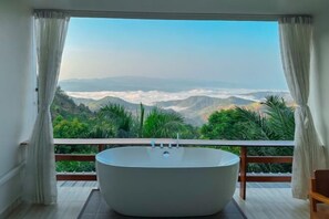 A modern bathroom with a freestanding bathtub, large windows, and a view of a mountainous landscape. - Masora Doichang (Mae Suai)