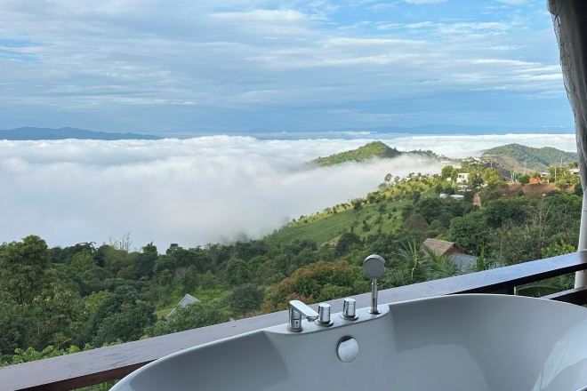 A bathtub with a view of a mountainous landscape and clouds below.