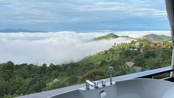 A bathtub with a view of a mountainous landscape and clouds below.