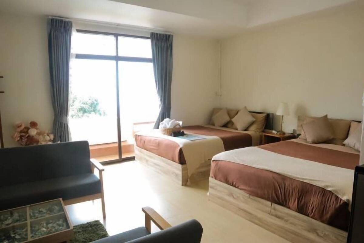 A hotel room with two beds, a sofa, a small table, and a window with curtains.
