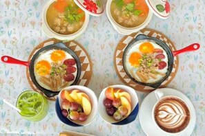 Une table avec quatre bols de soupe, deux bols de fruits, un verre de boisson verte et une tasse de café décorée avec un motif en latte art.