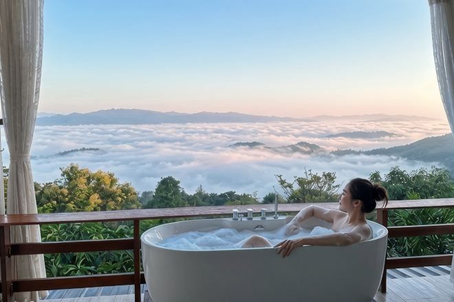 A person relaxing in a bathtub with a view of a mountainous landscape and clouds.
