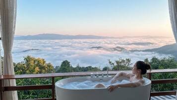 A person relaxing in a bathtub with a view of a mountainous landscape and clouds.