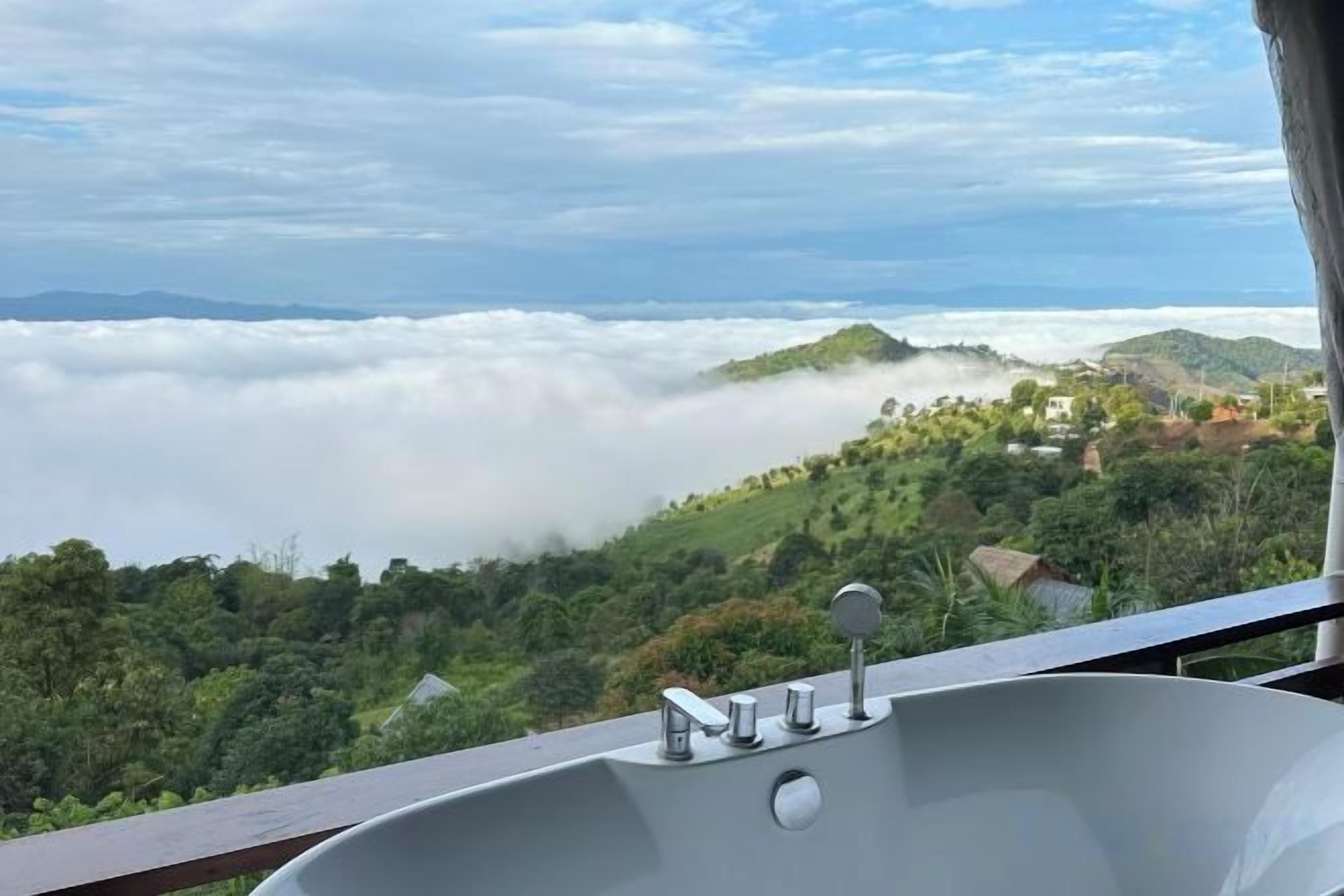 A bathtub with a view of a mountainous landscape and clouds.