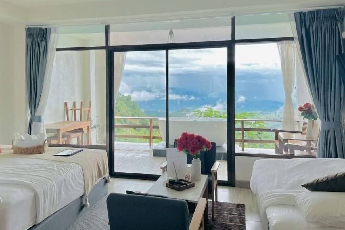 A hotel room with two beds, a desk, and a balcony with a view of the landscape.