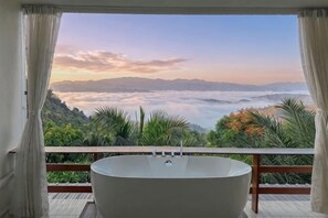 Une salle de bain avec une baignoire, une vue sur un paysage montagneux et un balcon agrémenté de plantes.