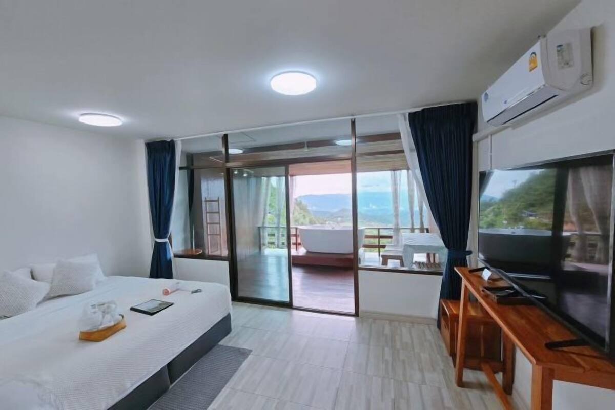 A hotel room with a bed, a TV, a desk, and a balcony with a view.