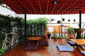 An outdoor patio with a wooden table and chairs, surrounded by potted plants and a bicycle. - Studio251 HOUSE (Lang Suan)