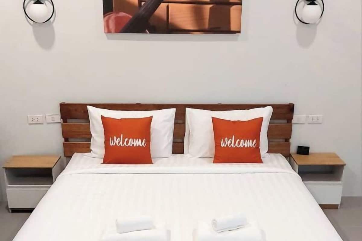 A neatly made bed with white bedding and two orange pillows with "welcome" text, flanked by two bedside tables with lamps.