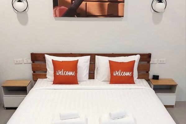 A neatly made bed with white bedding and two orange pillows with "welcome" text, flanked by two bedside tables with lamps.