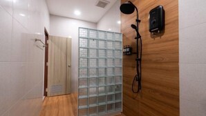 A modern bathroom with a glass shower enclosure, wooden panel walls, and a handheld showerhead. - Studio251 HOUSE (Lang Suan)