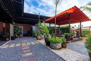 Un espace extérieur doté d’un coin salon abrité, de plantes en pot et d’un chemin menant à l’entrée d’un bâtiment.
