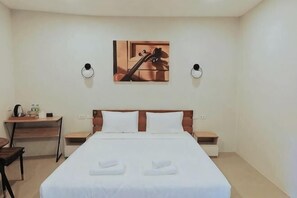 A hotel room with a bed, bedside tables, a desk, a chair, and a wall-mounted picture.