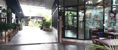 An indoor space with a covered walkway, potted plants, and a seating area with tables and chairs.