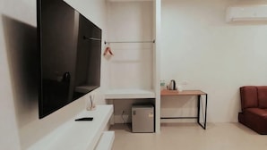 A modern living room with a flat-screen TV, a small table, a red sofa, and a compact refrigerator. - Studio251 HOUSE (Lang Suan)