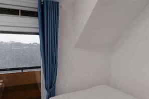A room with a bed, a window with a view of a cityscape, and a blue curtain.