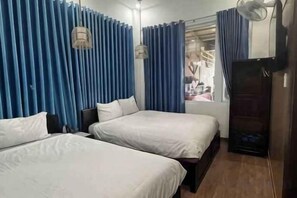A hotel room with two beds, a wardrobe, a fan, and curtains. - Michelia Valley Hotel (Dalat)