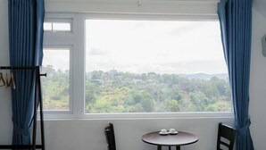 A room with a large window, two chairs, a small table, and a coat rack. - Michelia Valley Hotel (Dalat)