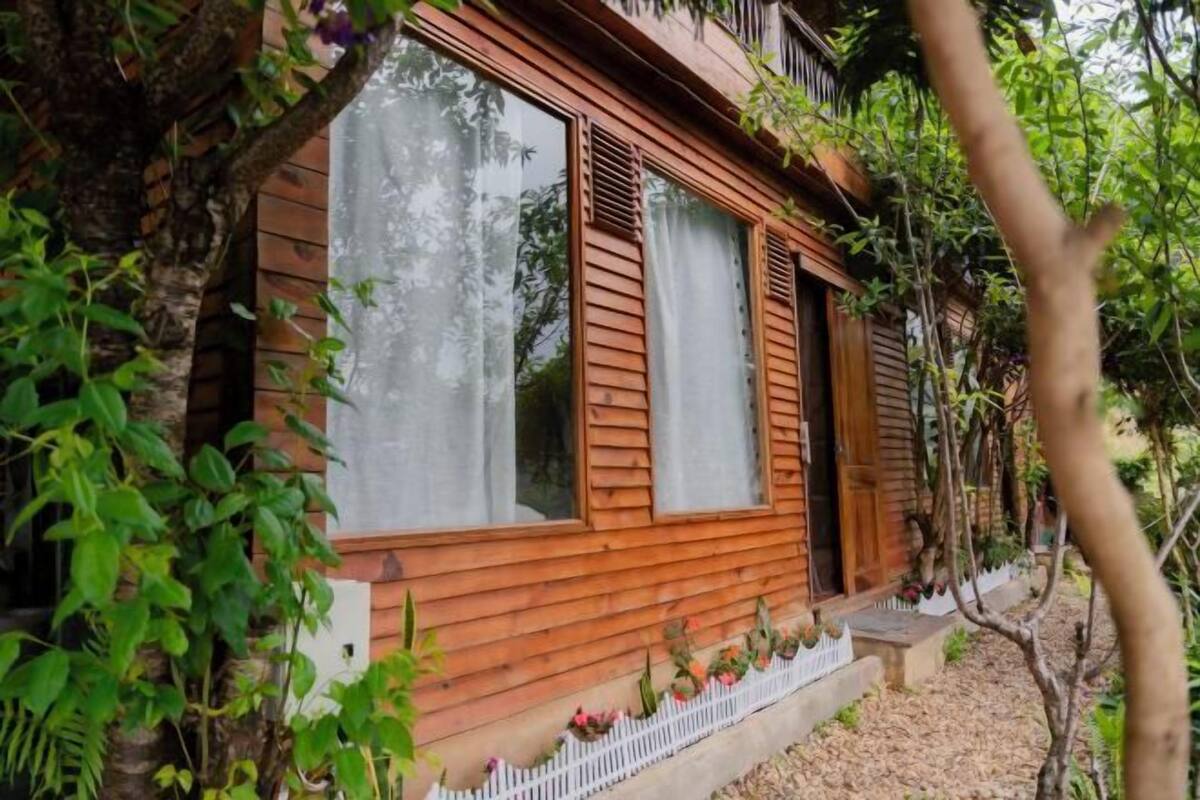 A wooden cabin with large windows, a white picket fence, and a small porch area.
