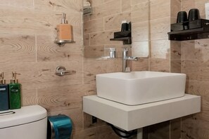 A bathroom with a white sink, a toilet, and a towel dispenser. - Michelia Valley Hotel (Dalat)