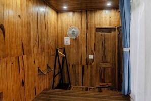 A wooden-paneled room with a door, a fan, and a small shelf. - Michelia Valley Hotel (Dalat)