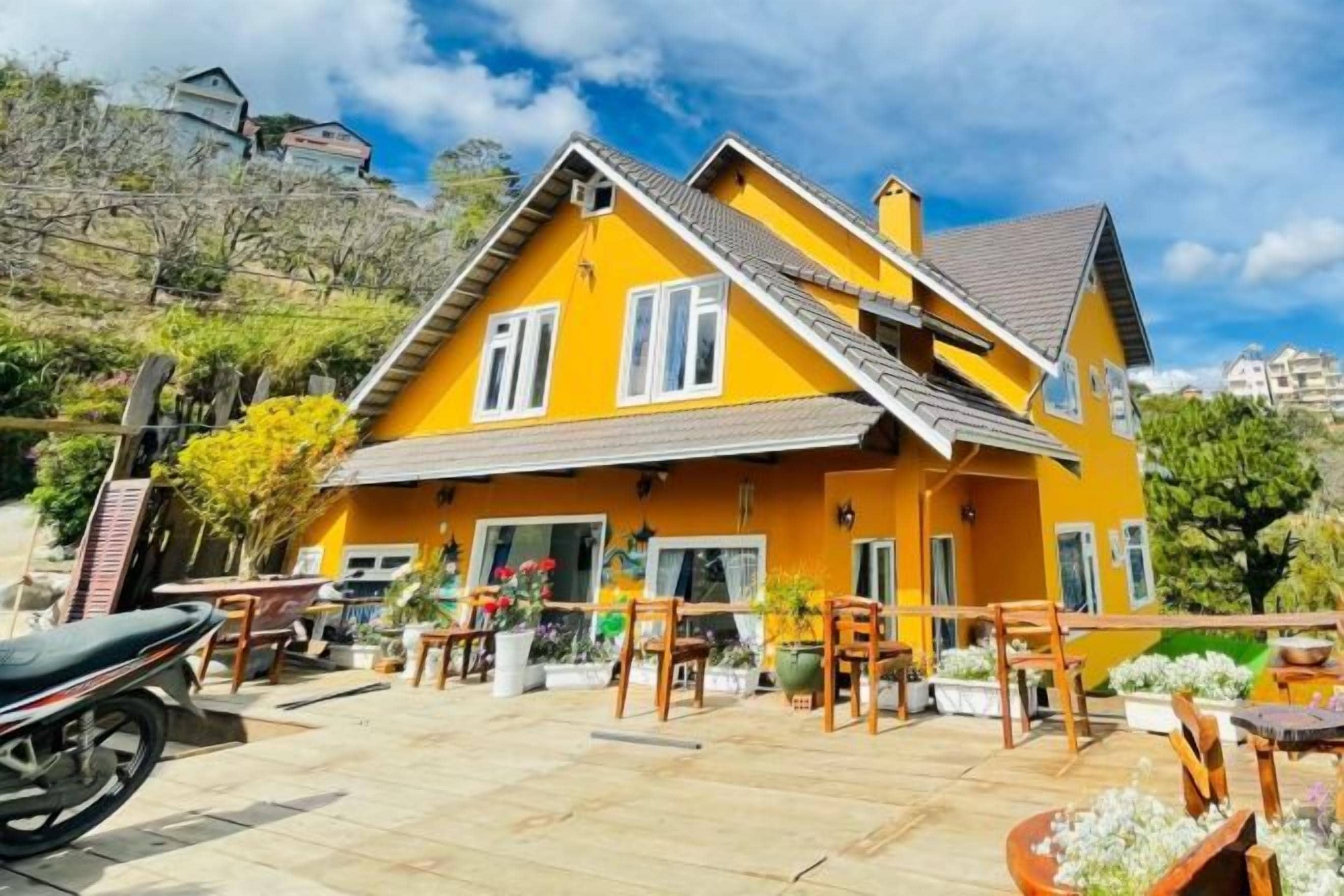A yellow house with a tiled patio, outdoor furniture, and a motorcycle parked in front.